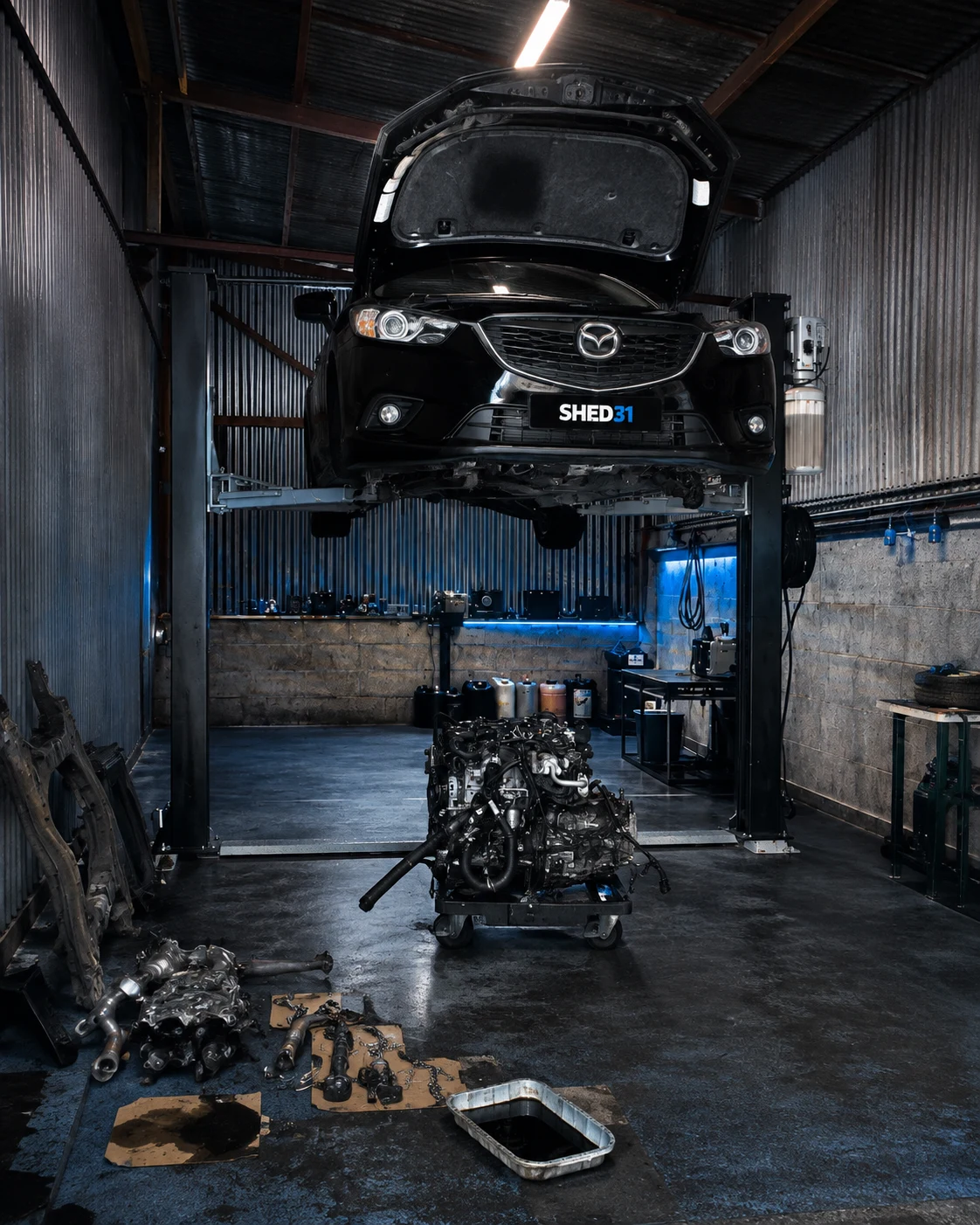 Black Mazda in the Shed 31 workshop with bonnet open and engine removed